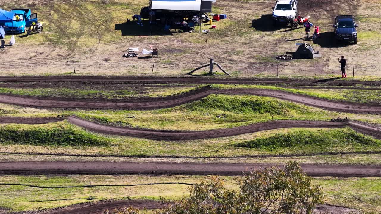 Child on dirt bike rides motocross track, sunny outdoor setting, aerial wide shot, steady camera