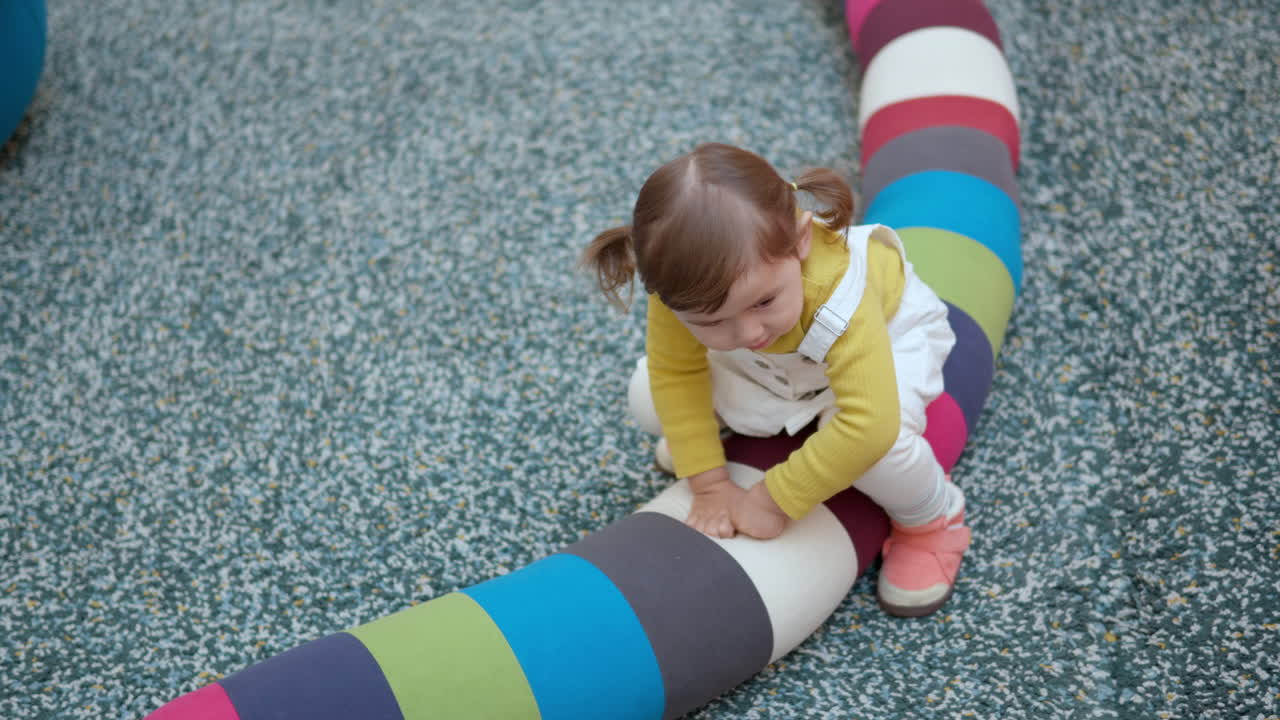 Happy 3-Year-Old Toddler Girl Sitting On Colorful Soft Long Pillow At The Play Area Inside A Shopping Mall