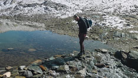 solo male hiker stepping over rocks crossing shallow stream on top of cima fontana in valmalenco