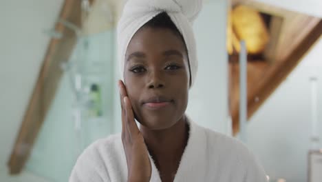 portrait of african american attractive woman taking care of face and looking at camera in bathroom