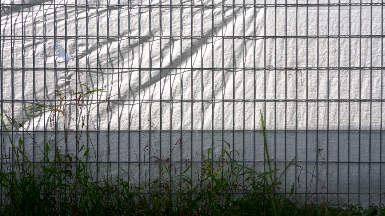 Skygger av metallgittergjerde på hvitt plastmateriale