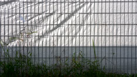 Schatten-Des-Metallgitterzauns-Auf-Weißem-Plastikmaterial.-Windiger-Tag