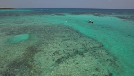 Aerial-View-of-tropical-waters-and-shallow-coral-reef-with-small-boats-anchored-off-shore