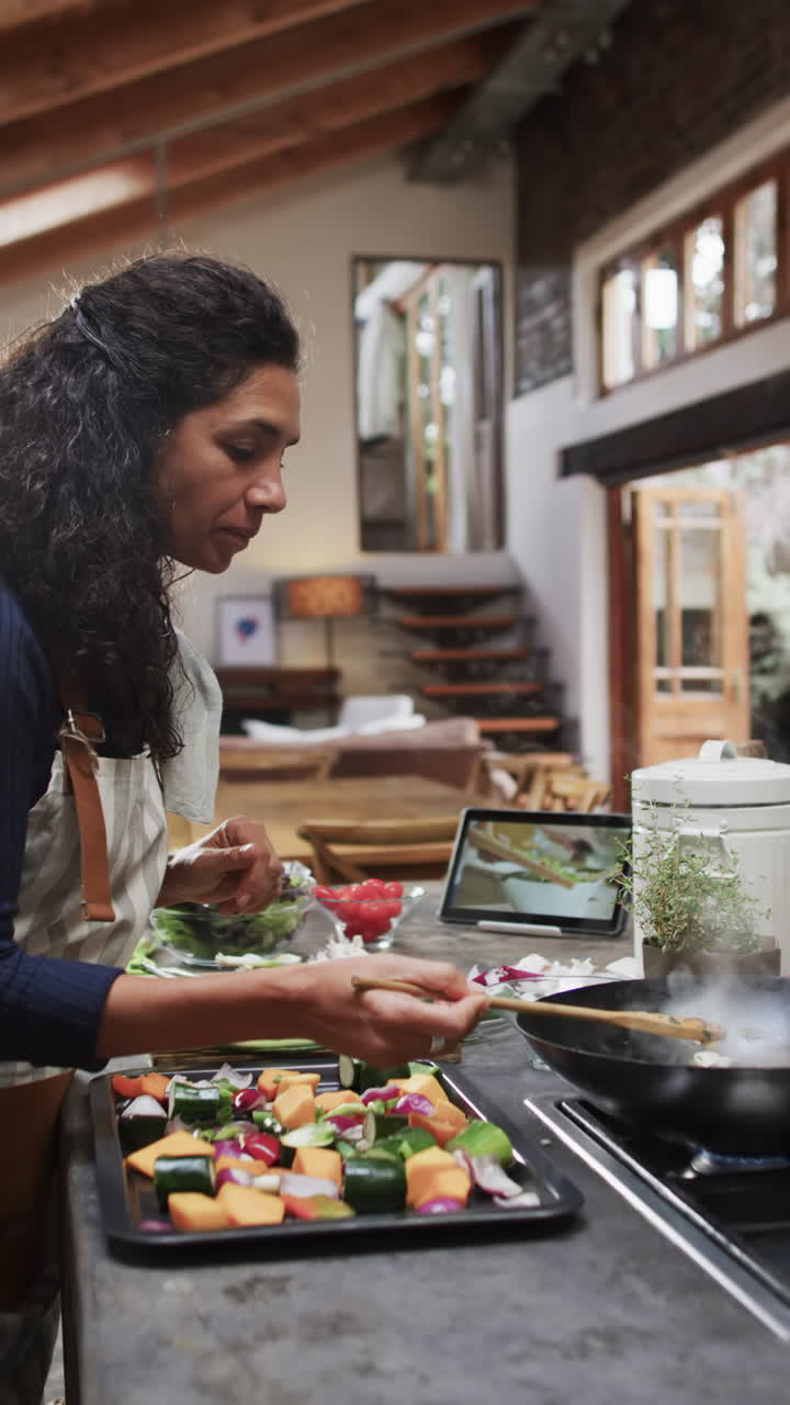 Vertical video of biracial woman in apron preparing meal in kitchen, slow motion