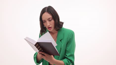 woman in green jacket reading a book with a surprised expression