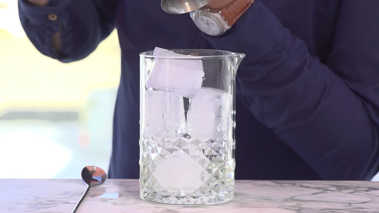 barman vertiendo bebida alcohólica en un vaso con hielo
