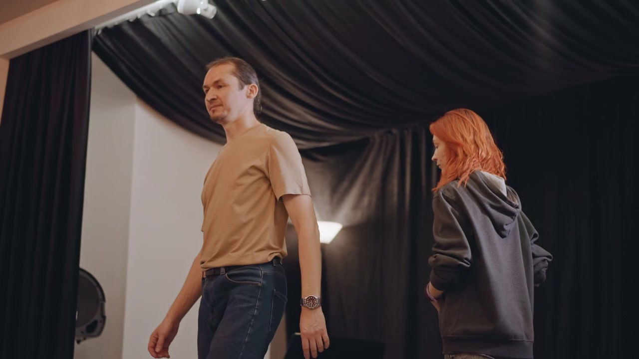 Studio rehearsal with vocal coach redhead singer small rehearsal room black curtains warm lamp light musicians adjusting posture coach giving notes student listening director checking cues casual