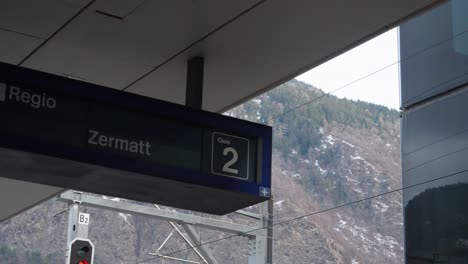 steady shot of train station, train departing towards zermatt, name placed under the roof