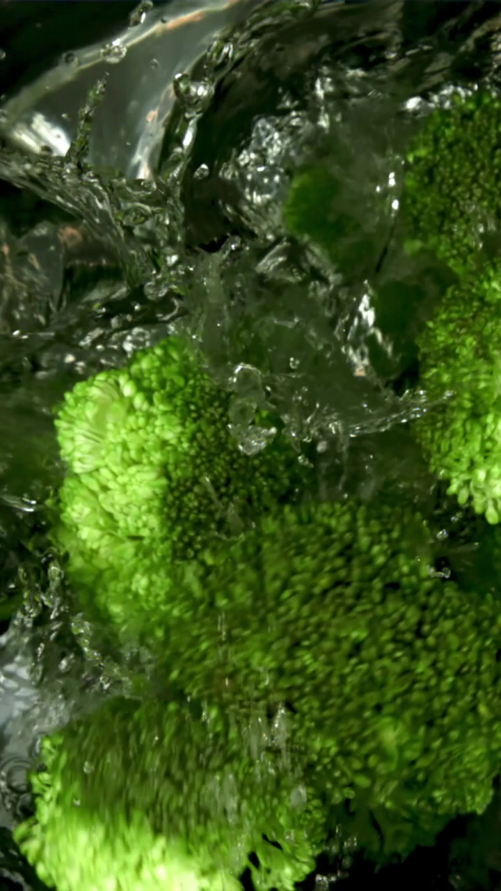 Cimette di broccoli freschi e verdi che vengono lavate con acqua che schizza