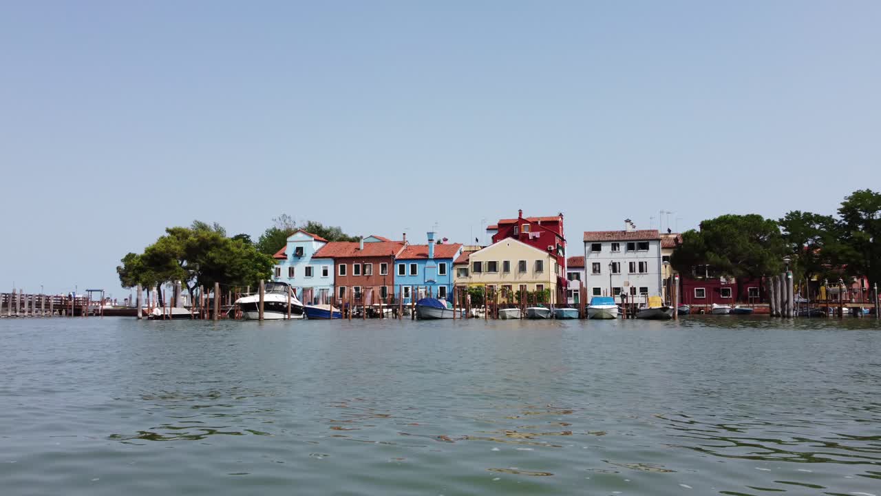 burano venice italy 드론은 밝은 여름날 다채로운 집에 접근하기 위해 물 위를 낮게 날고 있습니다.