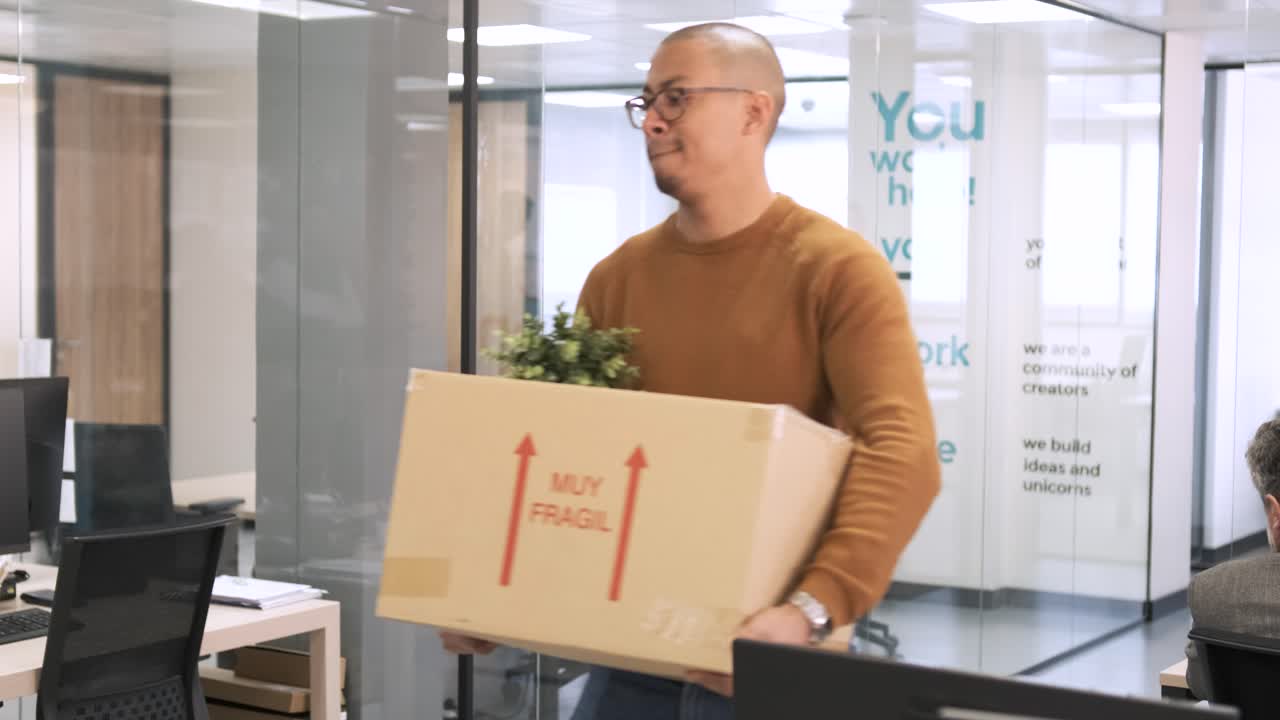 Hispanic man carrying cardboard box as he leaves creative workspace
