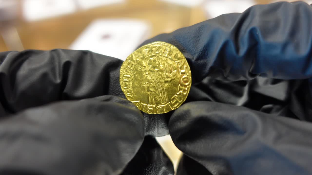 Collezionista che esamina una moneta d'oro portoghese dell'Età delle Scoperte.