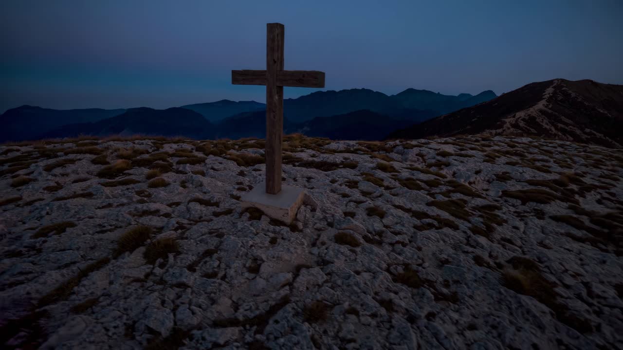 A low-angle video shot of a wooden cross on a rocky mountain at dusk, capturing a serene