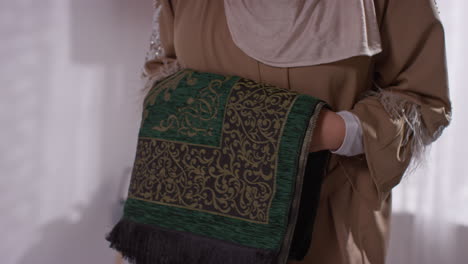 close up of muslim woman at home carrying prayer mat