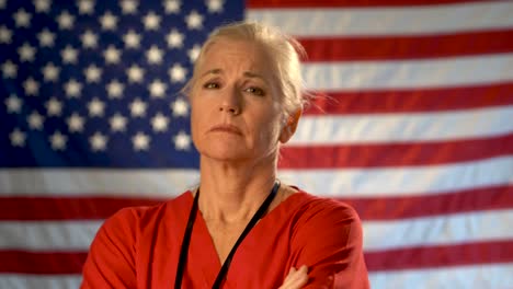 medium tight portrait of nurse looking extremely worried and sad with american flag behind her