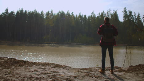 A-man-walks-along-a-path-in-a-park-near-a-lake-in-the-early-morning-in-the-autumn.-Man-Hill-Top.-Young-Man-Standing-On-Pier-With-Arms-Outstretched.-High-quality-4k-footage