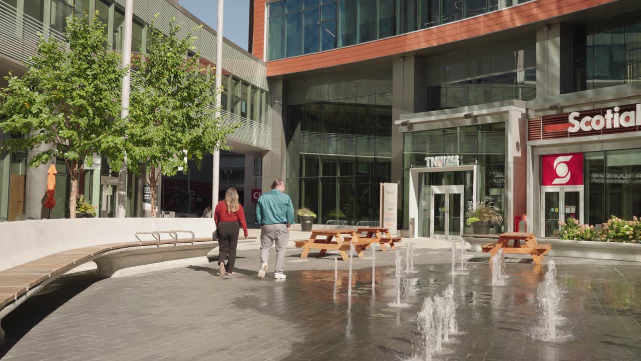Two people walk away in slow motion through True North Square in Winnipeg downtown