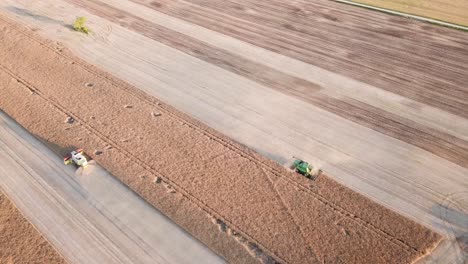 two combines harvesting grain crops from dry fields during a sunset in lithuania