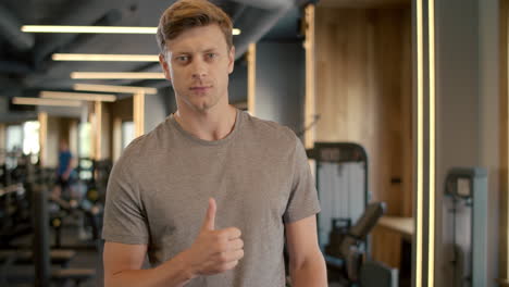 confident fitnessman showing thumb up in sport club. sportsman standing at gym