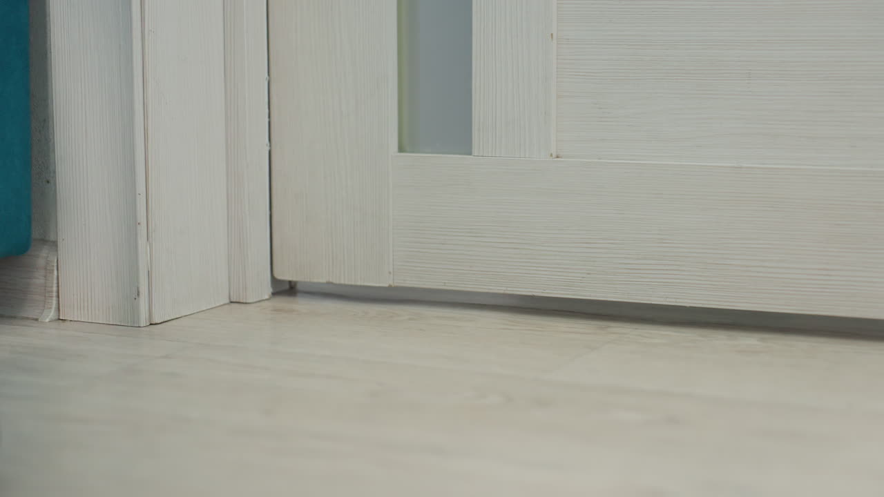 Grey Slippers Stepping Inside Near Door Frame. Candid Closeup Of Denim Hem And Textured Slippers Crossing Threshold, Guest Arrival Atmosphere With Slow Shuffle On Light Hardwood And Cozy Interior