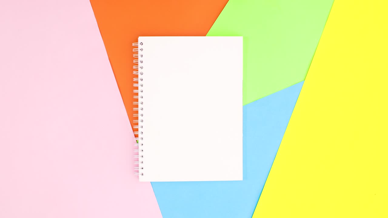 Colored pencils appear around open notebook on colorful theme. Stop motion