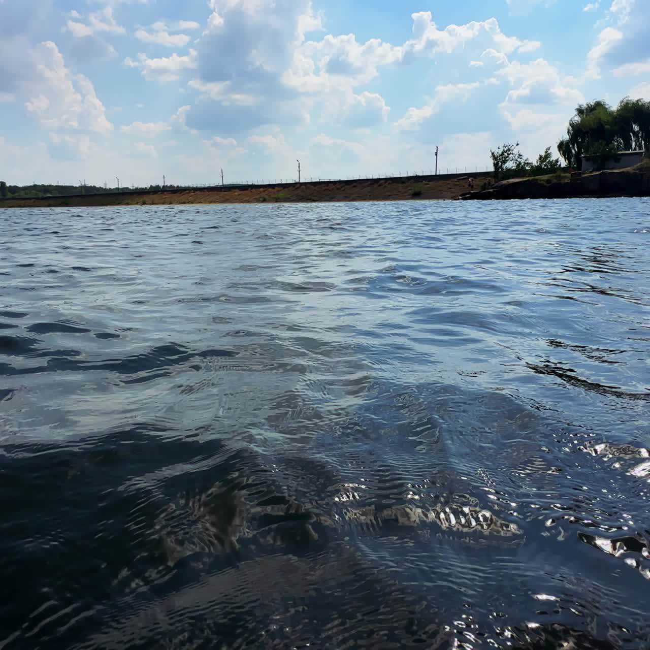 Uneven surface of river. Little waves move in the wind. Close up. Waterfront and sky at backdrop