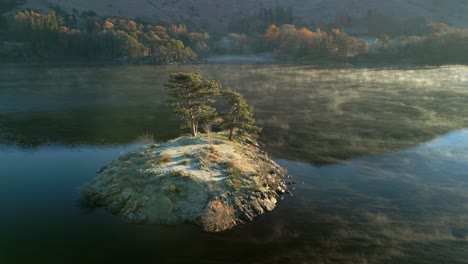 small island with trees in calm lake with moving mist at sunrise in autumn