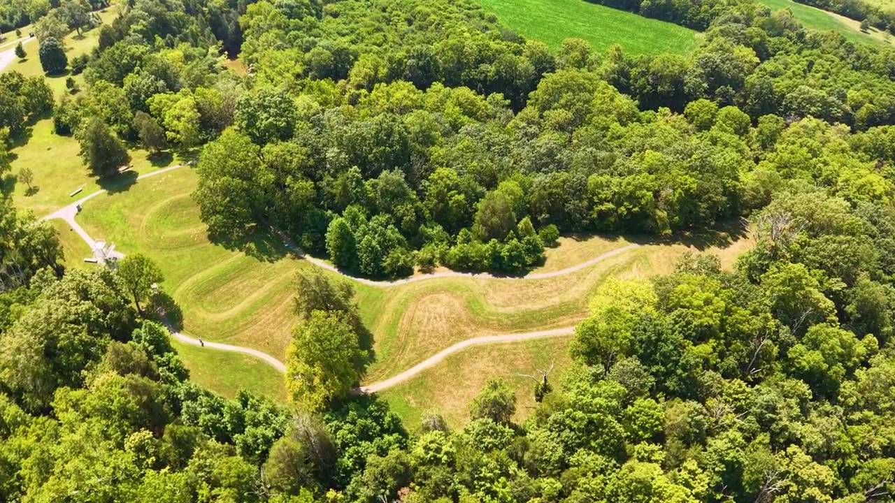 Letecký pohled na starobylou figurální mohylu v zalesněné oblasti s pěšími stezkami.