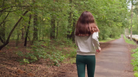 woman jogging along path in city park. exercising fitness and improving physical health in fresh air surrounded by different types of trees