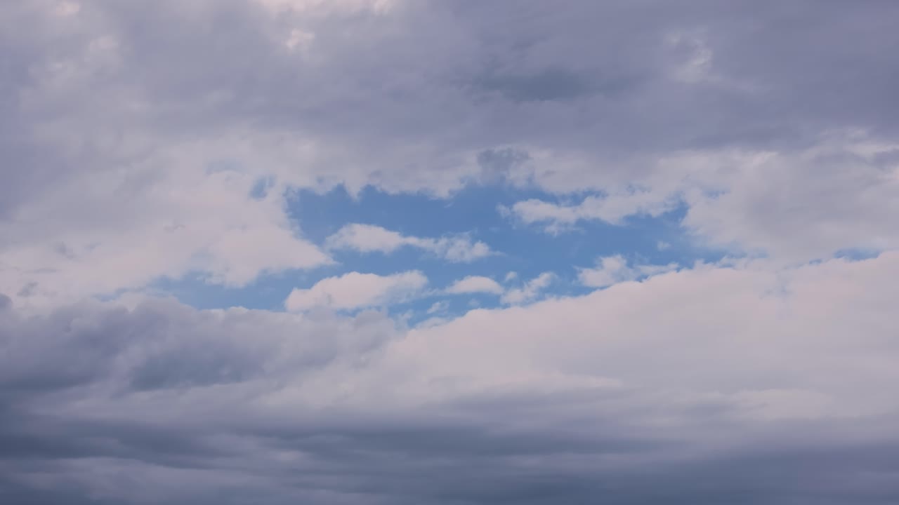 Static drone shot filmed at 167mm shows a dramatic accumulation of clouds, with a striking central opening that reveals a vivid, deep blue sky in stunning natural contrast