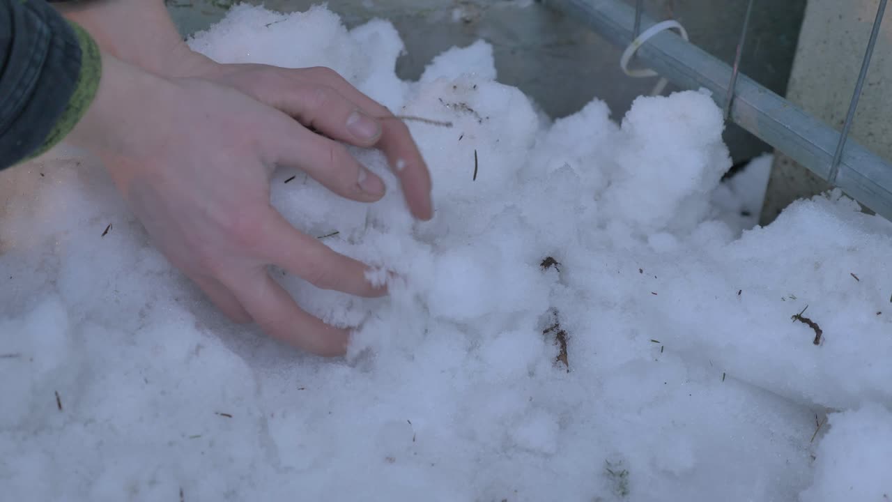 un hombre haciendo una bola de nieve con las manos desnudas sin guantes.