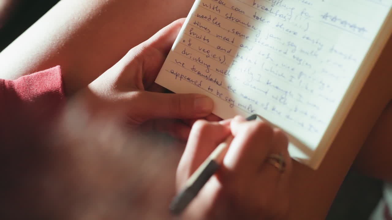 Closeup hands writing in notebook, warm natural light, soft film grain, pen tracing cursive lines, knee resting towel, silver ring on finger, personal diary entries, reflective mood, slow living