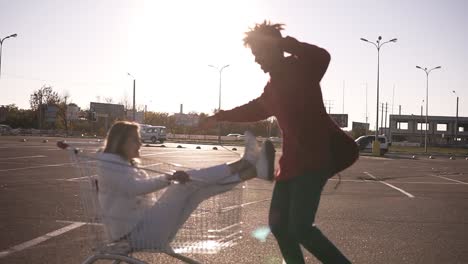 Feliz-Pareja-Joven-Montando-En-Carro-En-Un-Estacionamiento-Vacío-Del-Centro-Comercial,-Un-Amigo-Hipster-Se-Lo-Pasa-Bien-Después-De-Ir-De-Compras,-Una-Pareja-Enamorada-Montando-En-Un-Carrito-De-Compras,-Multirracial