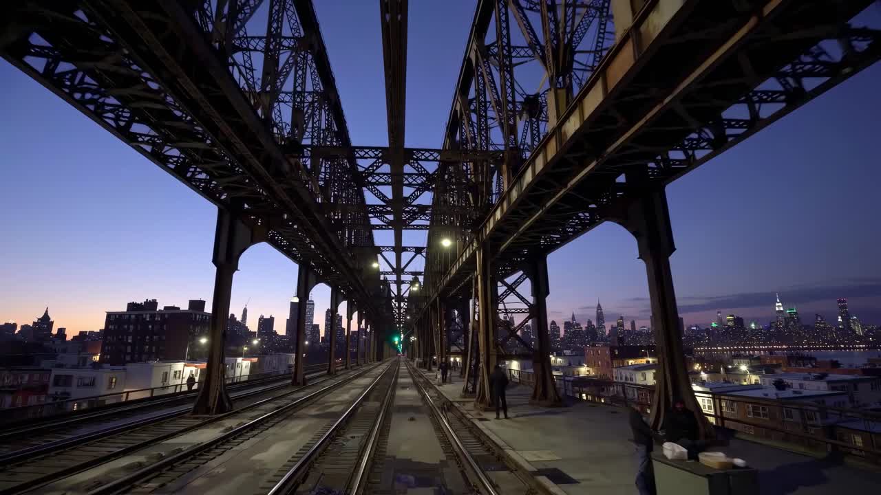 Video captures a symmetrical view under a steel bridge at dusk, showcasing urban architecture
