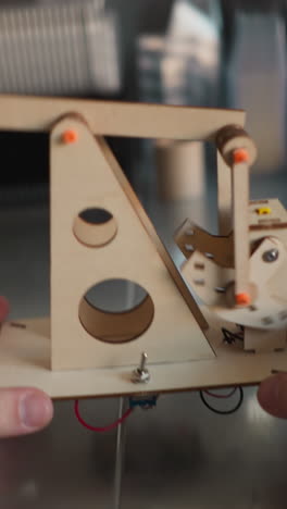 vídeo de manos levantando un modelo de bomba de aceite de madera en funcionamiento con motor a nivel de los ojos en un escritorio para inspección