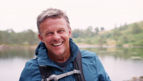 middle aged man standing on a camping holiday standing by a lake laughing, close up, lake district, uk