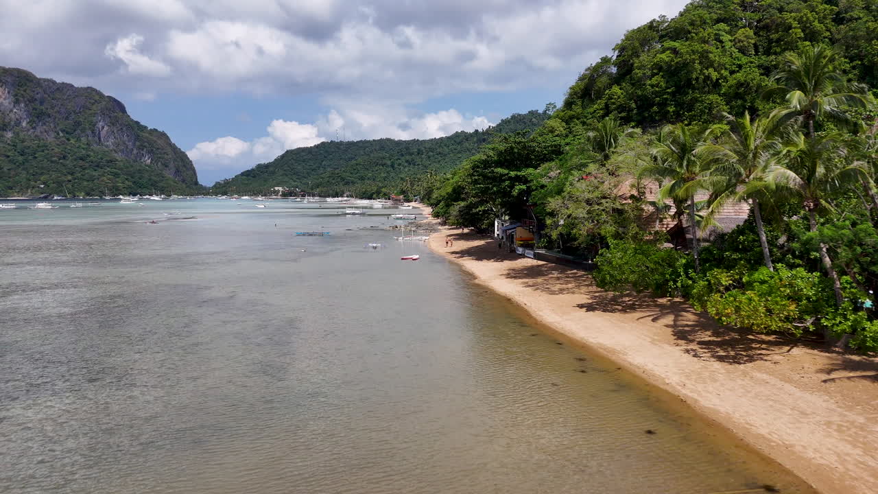 Aerial footage of boats in the harbor in Philippines, El Nido, featuring sparkling blue waters, white sandy beaches, and tropical forest landscapes.