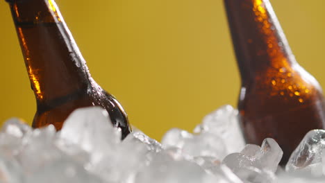 close up of person putting glass bottle of cold beer or soft drinks into ice filled bucket to chill against yellow background