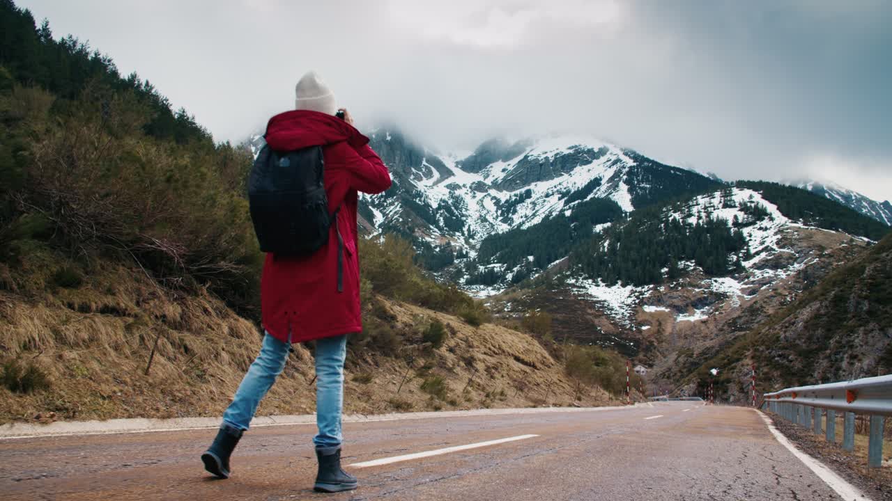 una joven fotógrafa de viajes camina por un camino vacío de montaña tomando fotos.