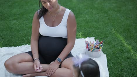 una madre y su hija pequeña se sientan en una manta en el patio trasero, participando en una actividad de dibujo juntos. la escena al aire libre captura un momento familiar pacífico, fomentando la creatividad y el vínculo.