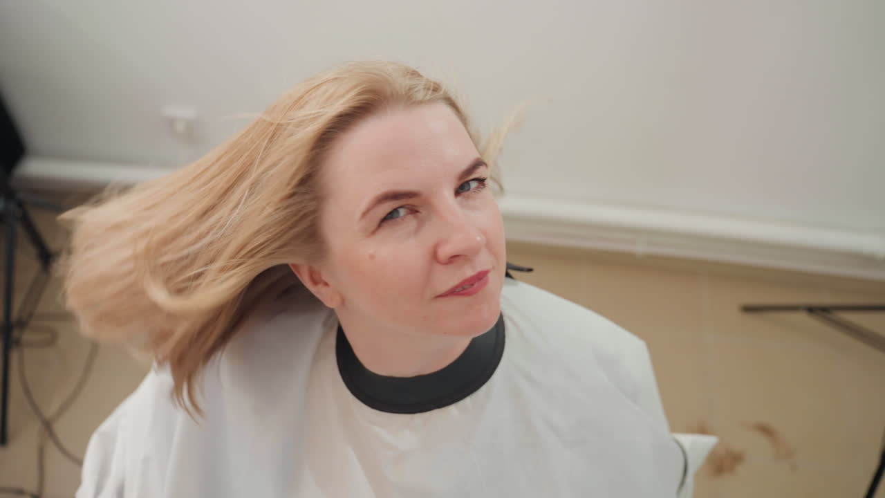 mujer caucásica rubia sonriendo después de un corte de pelo, mano del estilista visible mientras cae la capa, luz natural suave y movimiento delicado resaltan el bob moderno y las puntas pulidas, primer plano sincero mostrando