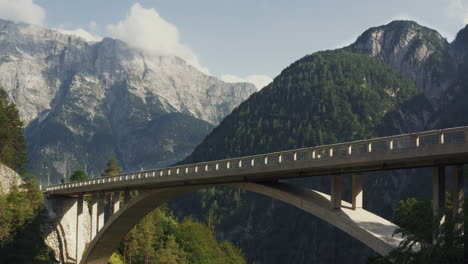 majestic arch bridge in sunny alpine landscape. towering mountain range and lush green forests in the background. car with bicycle on rack crossing bridge. slovenia.
static.