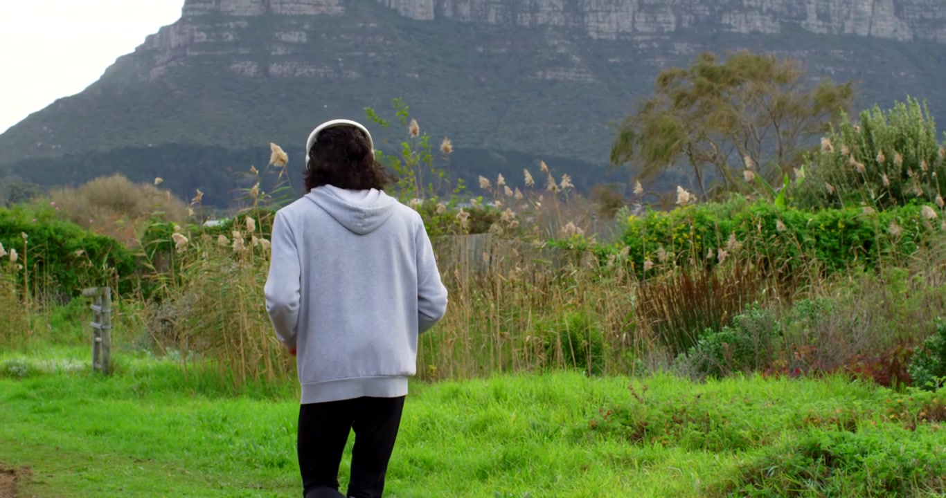African American man jogging entering left in hoodie and headset toward cliff trail exercising
