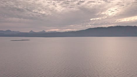 aerial flying over calm ocean at day near island in evening, no people