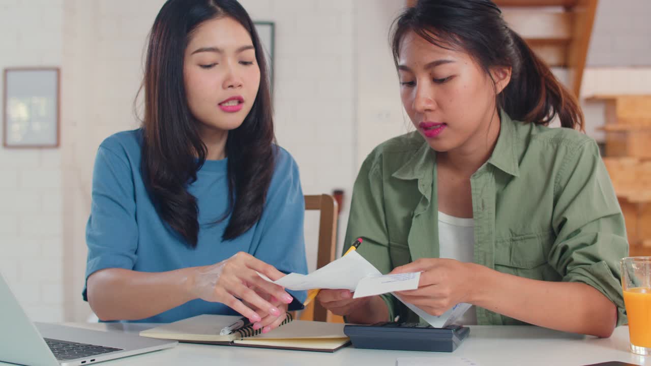 Business Asian Lesbian couple using calculator record budget, tax, financial document on laptop working in kitchen.