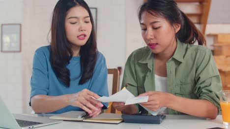 business asian lesbian couple using calculator record budget, tax, financial document on laptop working in kitchen.