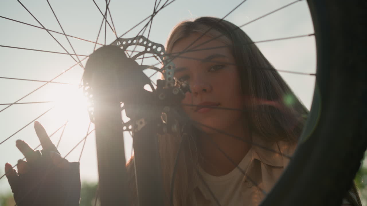 ciclista tocando suavemente la rueda de su bicicleta, radiando con una cálida sonrisa mientras la luz del sol brilla sobre ella y la rueda gira, este momento captura su alegría y conexión con el ciclismo