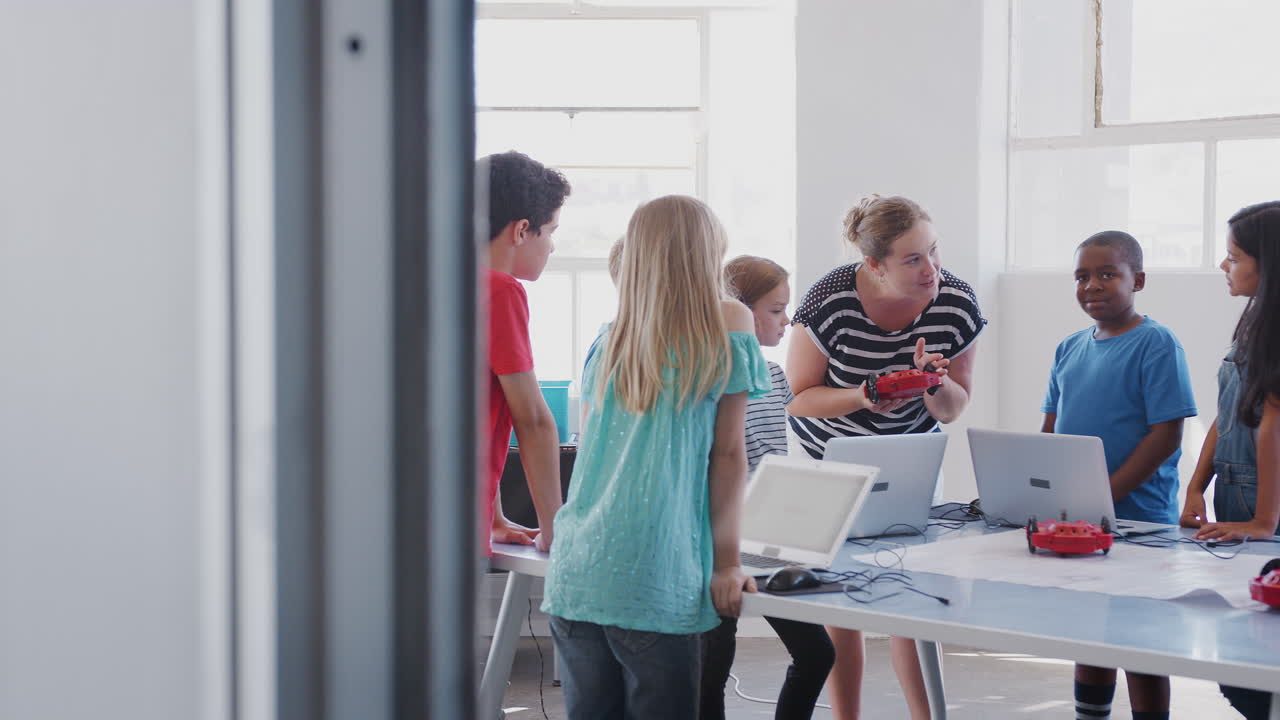 방과 후 컴퓨터 코딩 수업에서 여성 선생님과 함께 학생들이 로 ⁇  차량을 프로그래밍하는 법을 배우고 있습니다.