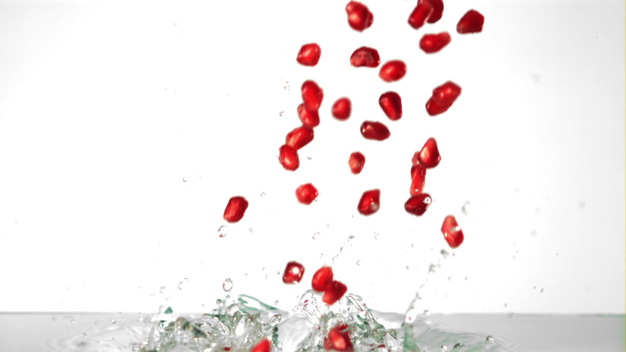 Red Pomegranate Seeds Falling and Splashing into Water