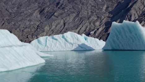 icebergs floating in glacial water with rocky mountains in background